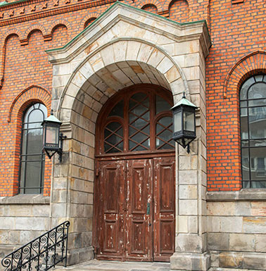 en kyrka av rött tegel med mintgrönt plåttak samt sockel och portal av granit